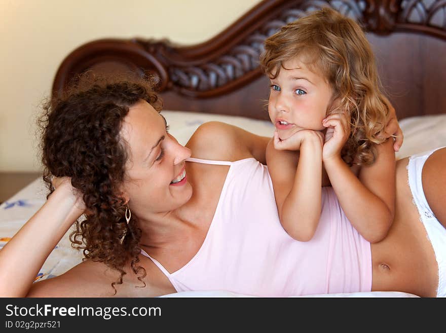 Young mother and daugther embracing on bed. little girl tells to mum story lying in bed