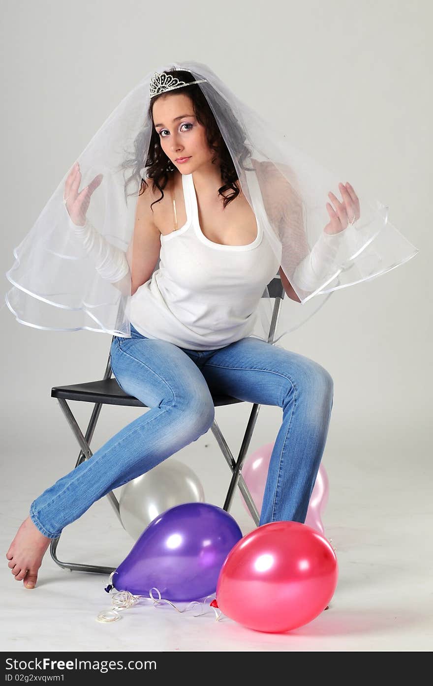 Portrait of the young girl sitting on a chair in jeans and a white vest. The bride in a veil prepares for wedding