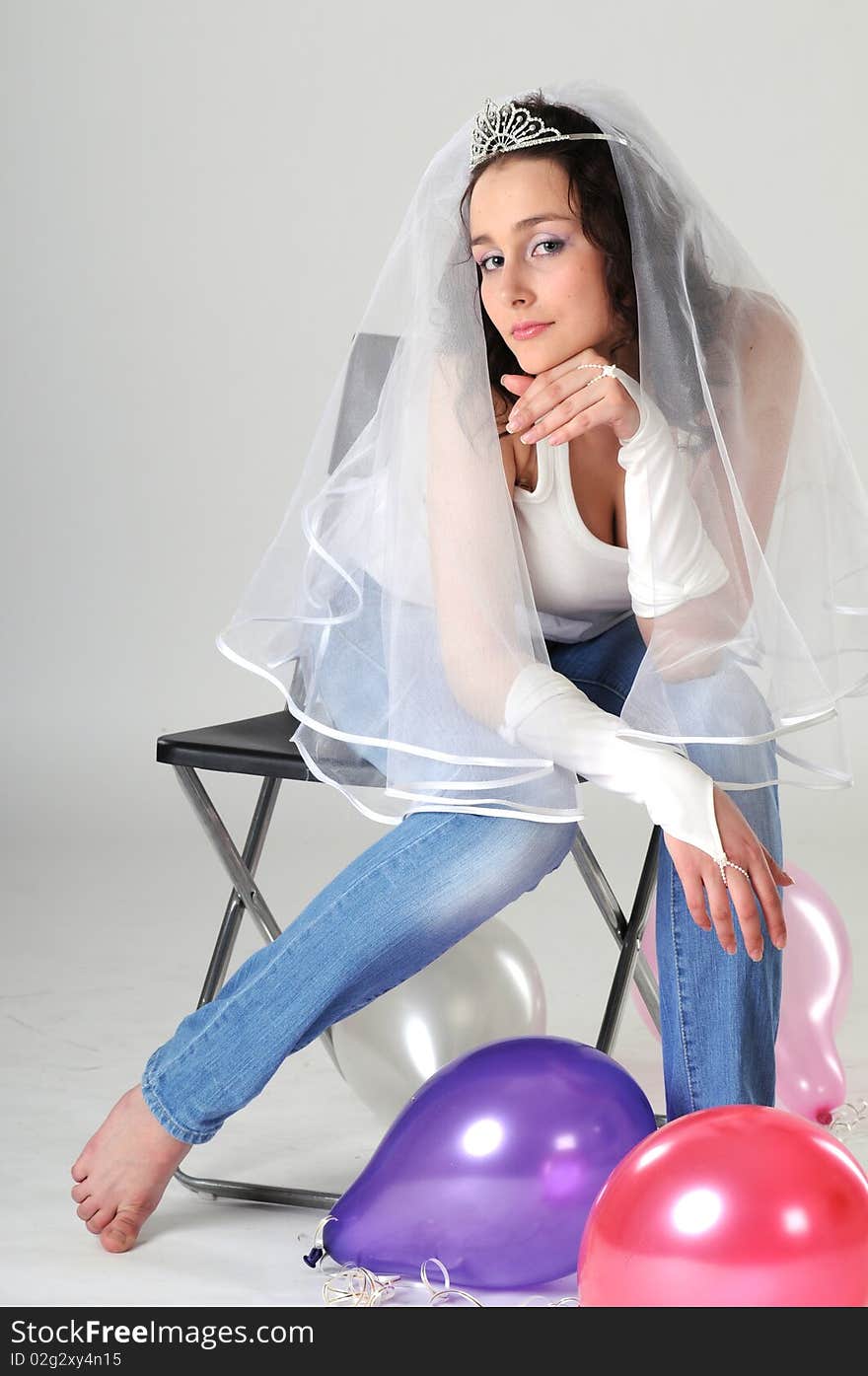 Portrait of the young girl sitting on a chair in jeans and a white vest. The bride in a veil prepares for wedding