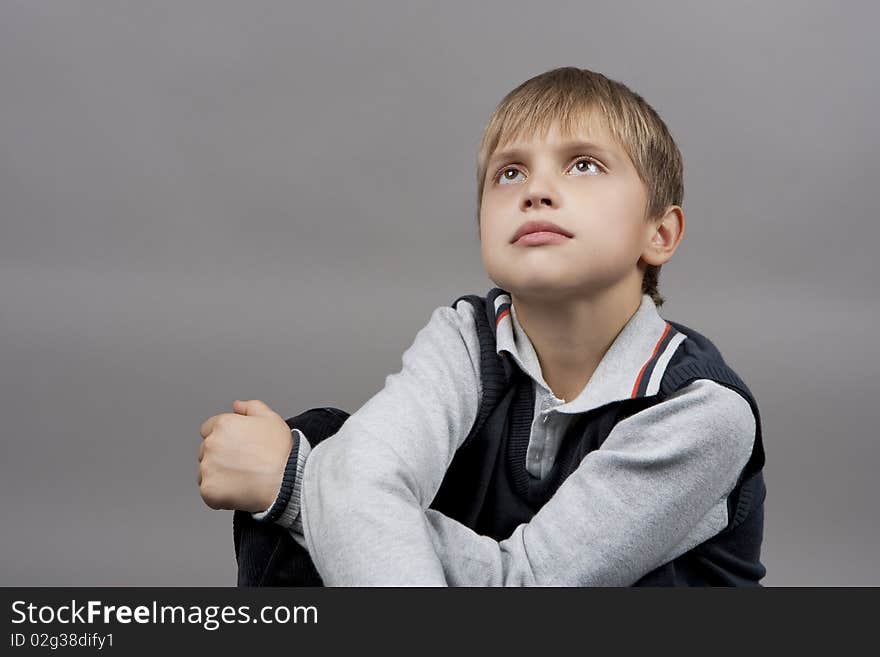 Dreaming and relaxing blond caucasian teenager boy with eyes lifted and hands crossed in front isolated over gray background. Dreaming and relaxing blond caucasian teenager boy with eyes lifted and hands crossed in front isolated over gray background