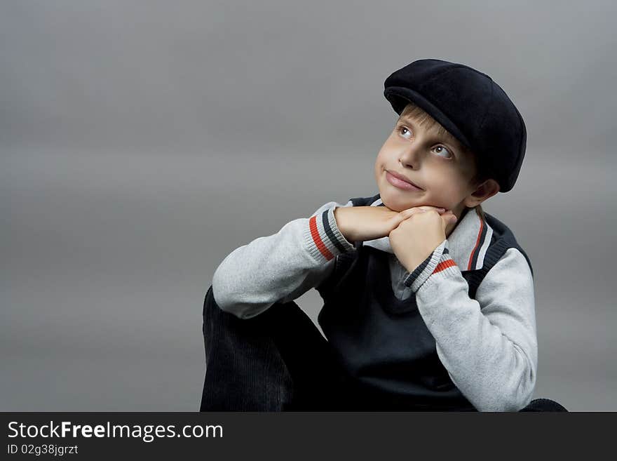 Cute teenager boy in old school cap sitting with hands crossed in front and smiling with natural nice smile isolated over gray background. Cute teenager boy in old school cap sitting with hands crossed in front and smiling with natural nice smile isolated over gray background