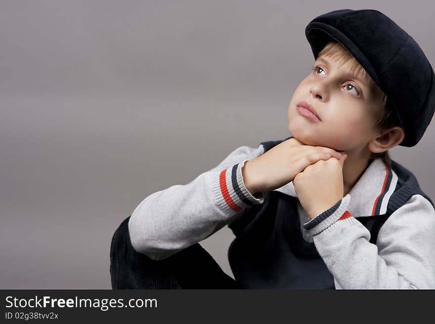 Relaxing and calm teenager boy in old cap sitting with hands crossed in front and looking up isolated over gray background. Relaxing and calm teenager boy in old cap sitting with hands crossed in front and looking up isolated over gray background