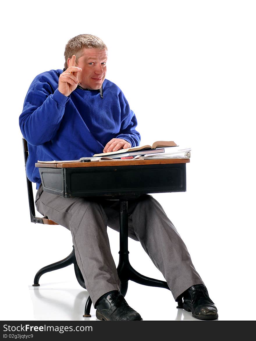 A mature adult student in a child-sized desk filled with books and papers, his hand shyly raised. Isolated on white. A mature adult student in a child-sized desk filled with books and papers, his hand shyly raised. Isolated on white.