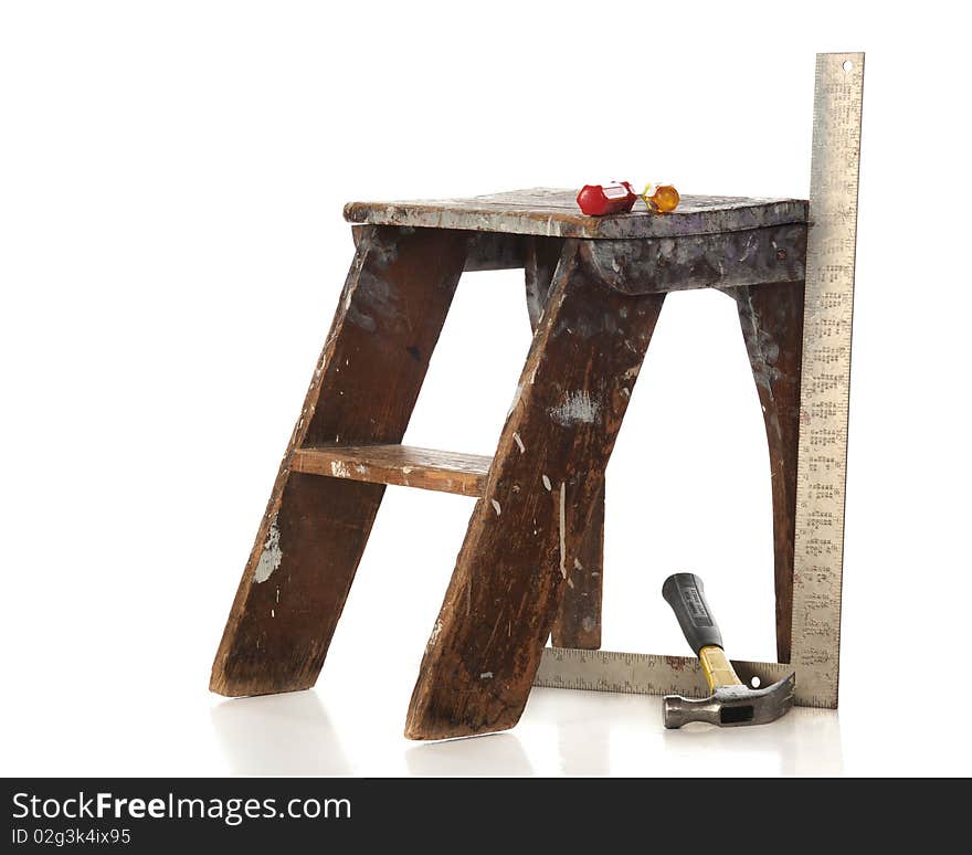 A hammer, square and a couple of screw drivers by a battered, old step stoool.  Isolated on white. A hammer, square and a couple of screw drivers by a battered, old step stoool.  Isolated on white.