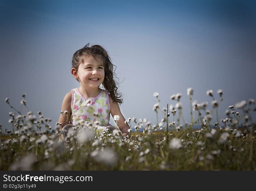 Little girl sitting in the white flowers smiling and happy. Little girl sitting in the white flowers smiling and happy