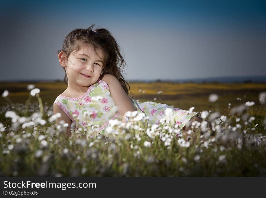 Little girl sitting in a field of white flowers smiling and happy. Little girl sitting in a field of white flowers smiling and happy