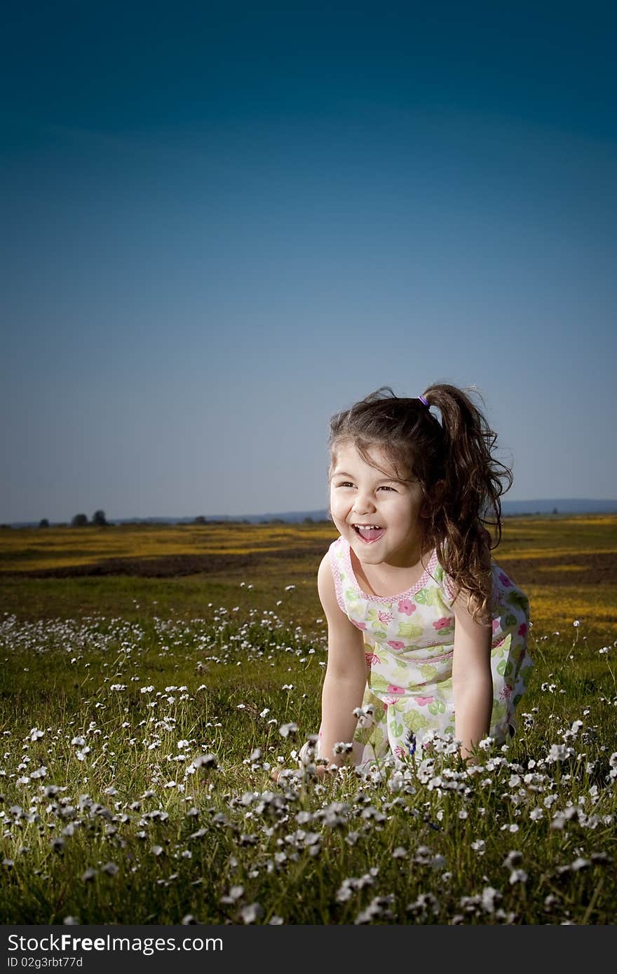 Little girl sitting in a field of white flowers laughing. Little girl sitting in a field of white flowers laughing