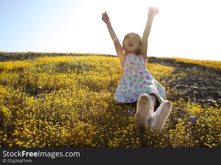 Little girl sitting in a field of yellow flowers with her hands in the air. Little girl sitting in a field of yellow flowers with her hands in the air