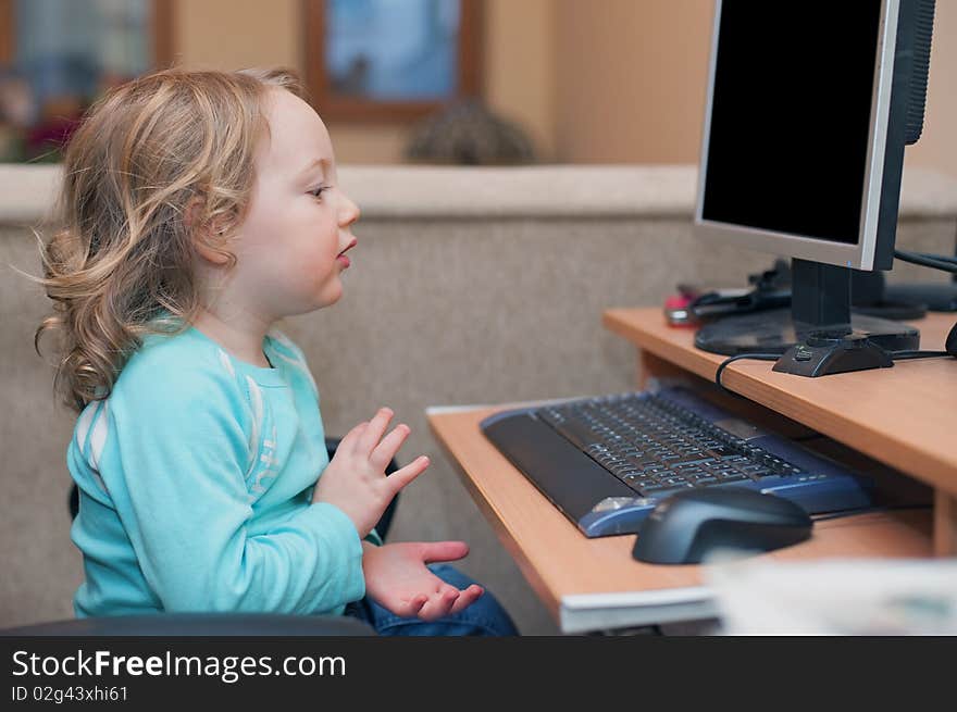 Little baby girl, sitting at a desktop computer at home, clapping hands with joy. Little baby girl, sitting at a desktop computer at home, clapping hands with joy