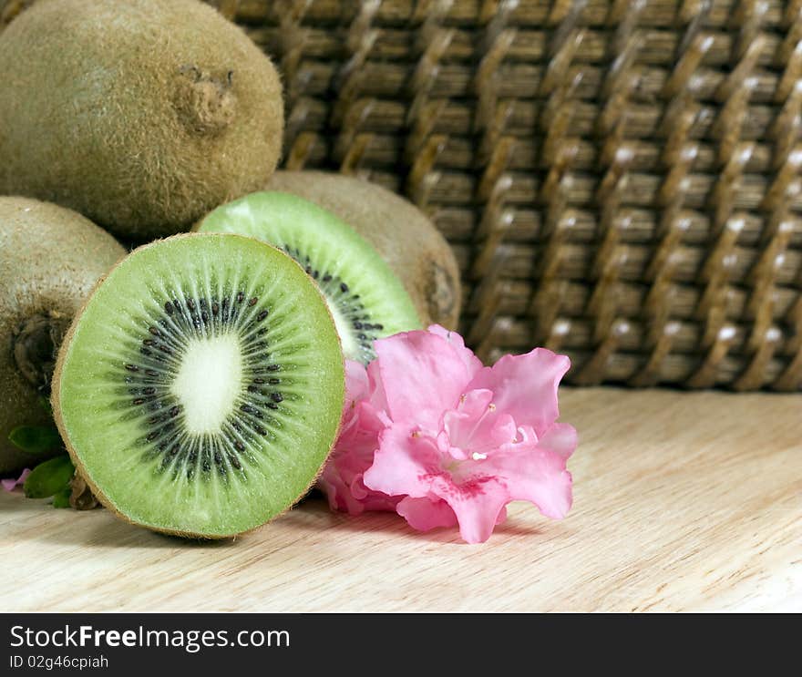 Cut kiwifruit on wood board with pink flower and wicker background