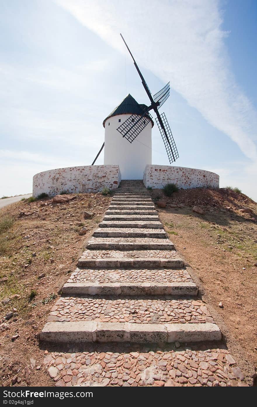 A lonely windmill standing at the end of some stairs, atop some hill.