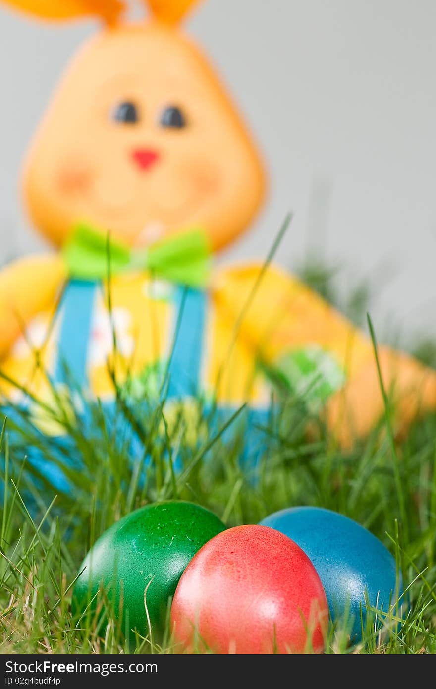 Toy easter bunny with colored eggs in the grass