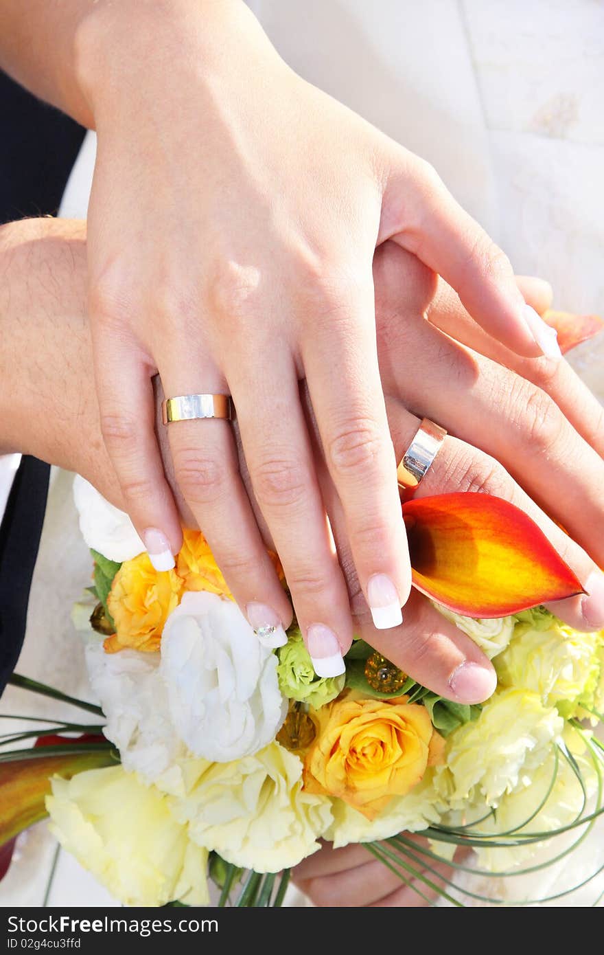 Newlywed couple holding hands over bouquet of flowers. Newlywed couple holding hands over bouquet of flowers.