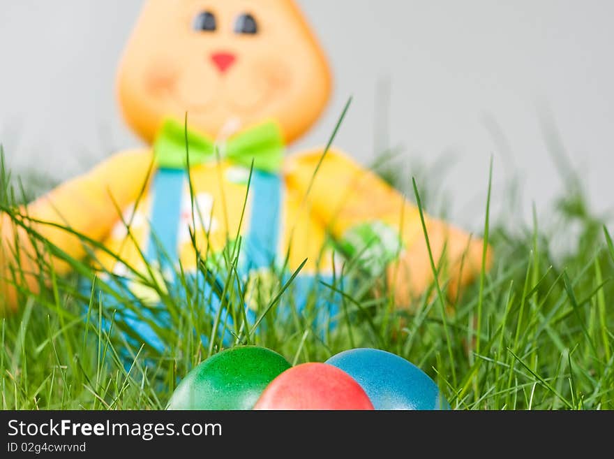 Toy easter bunny with colored eggs in the grass