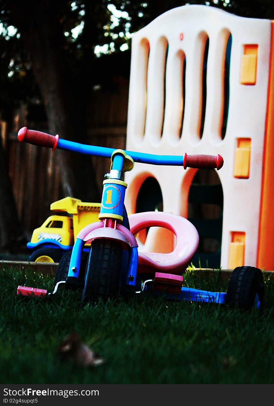 Tricycle with faded colors in a backyard with other toys in the background. Tricycle with faded colors in a backyard with other toys in the background.