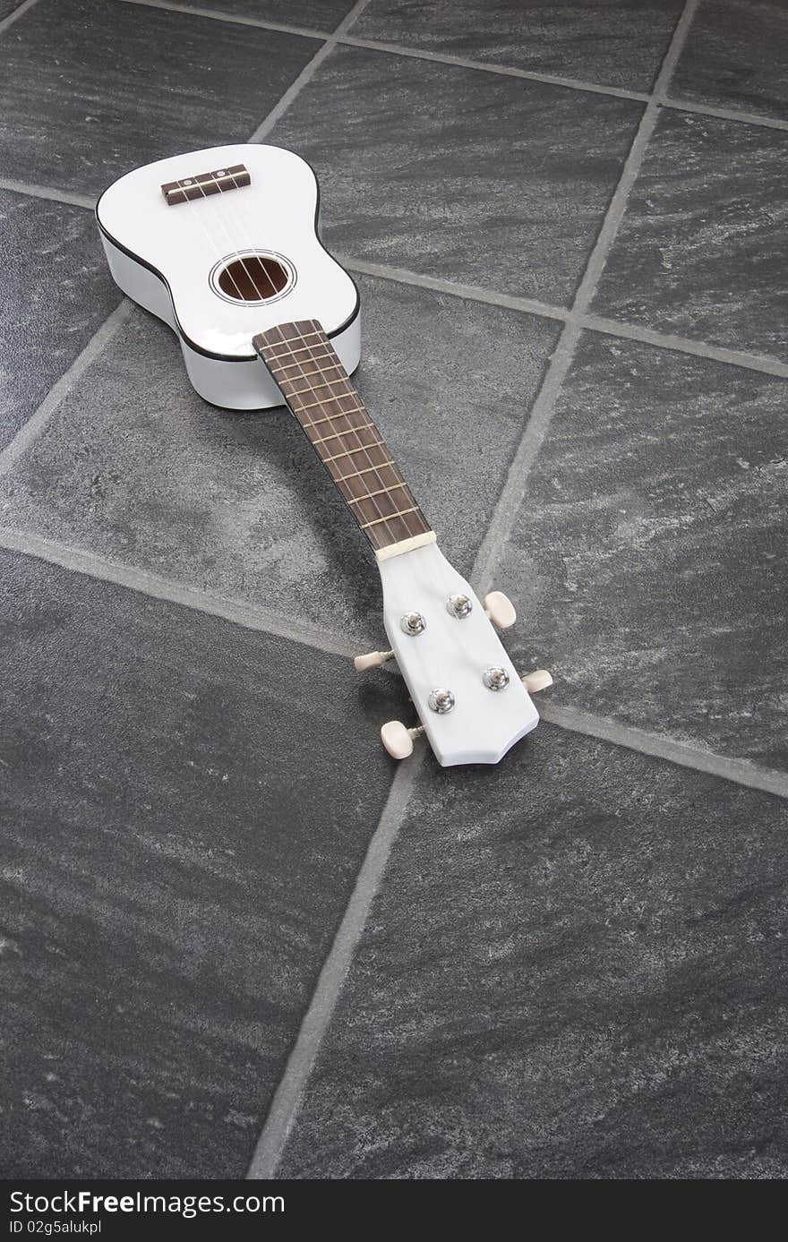 A white ukulele on a black/grey slate floor. A white ukulele on a black/grey slate floor.