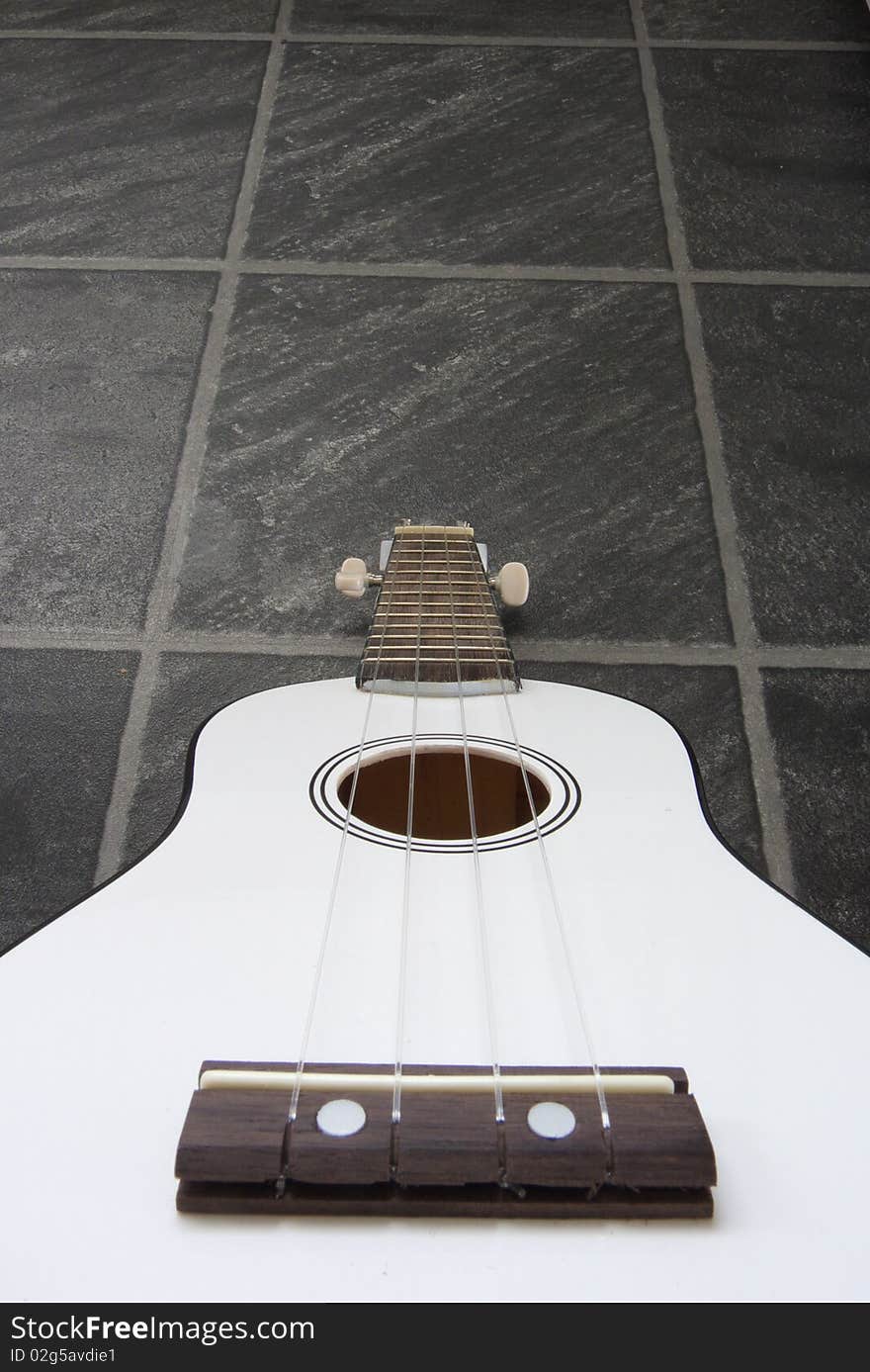 A white ukulele against a black/grey slate floor background. A white ukulele against a black/grey slate floor background.