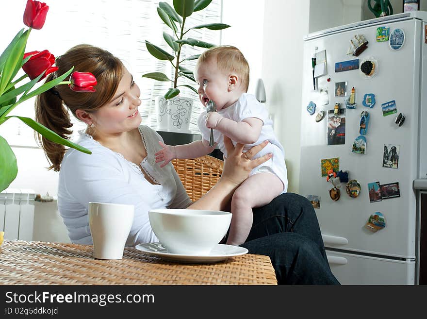 Young beautiful mother feeding her litlle cute baby daughter at the kitchen. Young beautiful mother feeding her litlle cute baby daughter at the kitchen