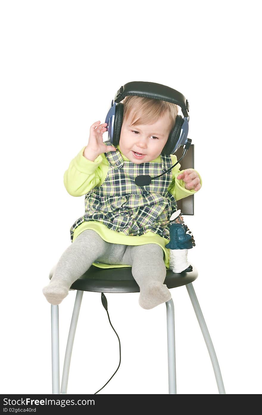 The happy small child sits on a chair in headset ear-phones with a microphone. Isolated on white background