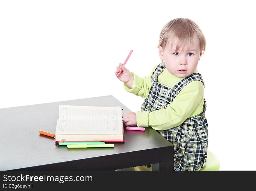 The little girl sits at a table and does a homework, draws in a notebook. It is isolated on a white background. The little girl sits at a table and does a homework, draws in a notebook. It is isolated on a white background