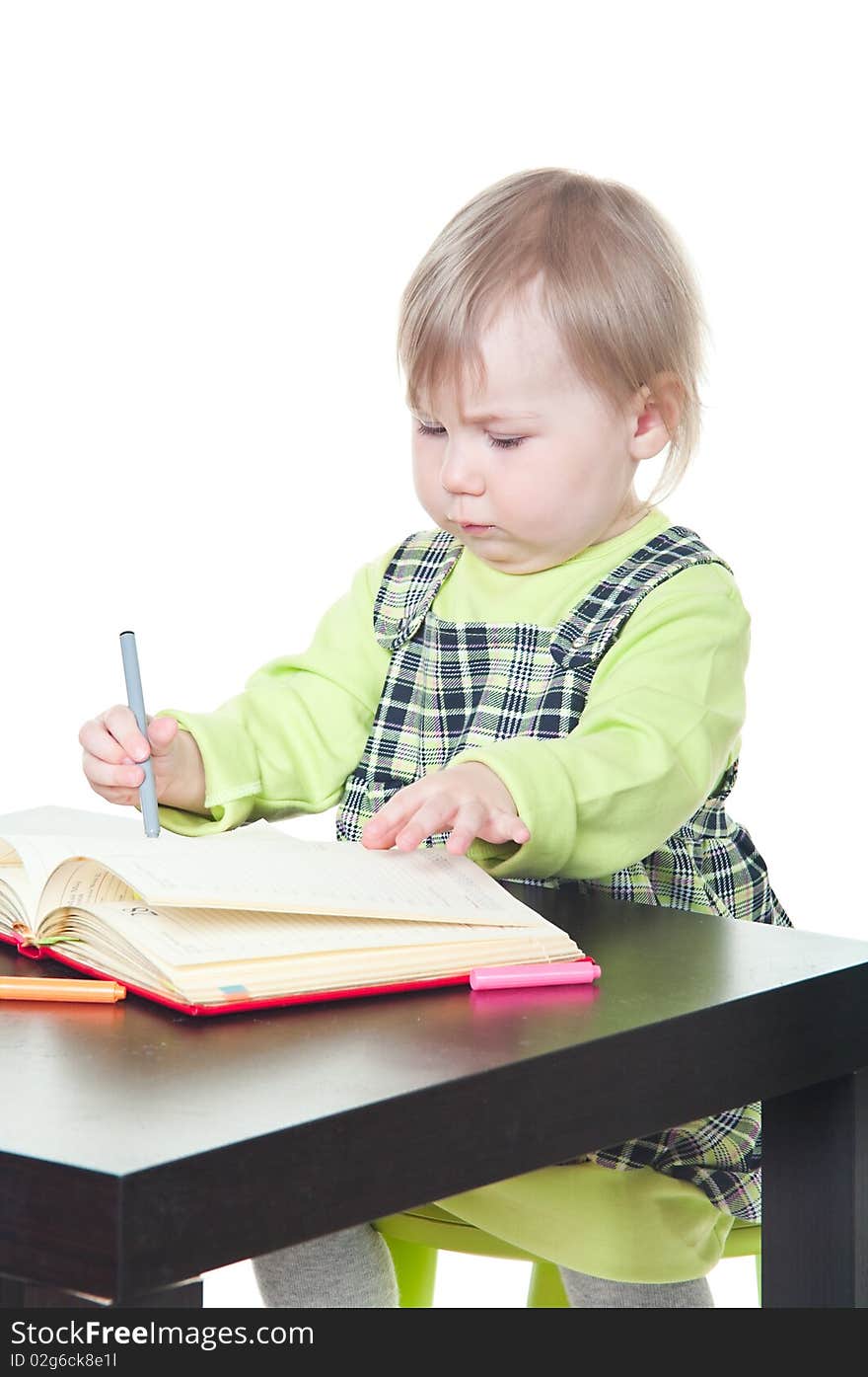 The little girl sits at a table and does a homework, draws in a notebook. It is isolated on a white background. The little girl sits at a table and does a homework, draws in a notebook. It is isolated on a white background