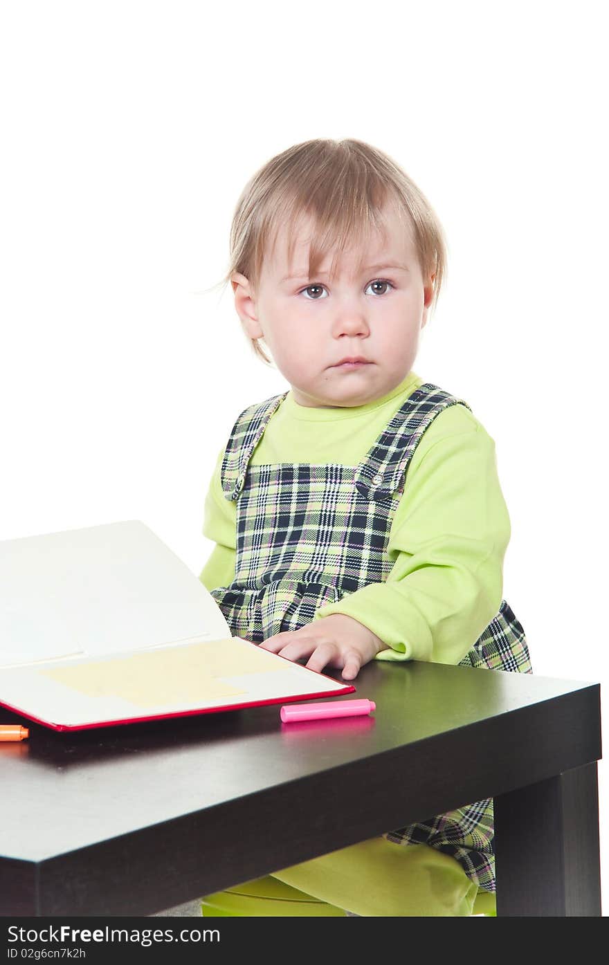 The little girl sits at a table and does a homework, draws in a notebook. It is isolated on a white background. The little girl sits at a table and does a homework, draws in a notebook. It is isolated on a white background