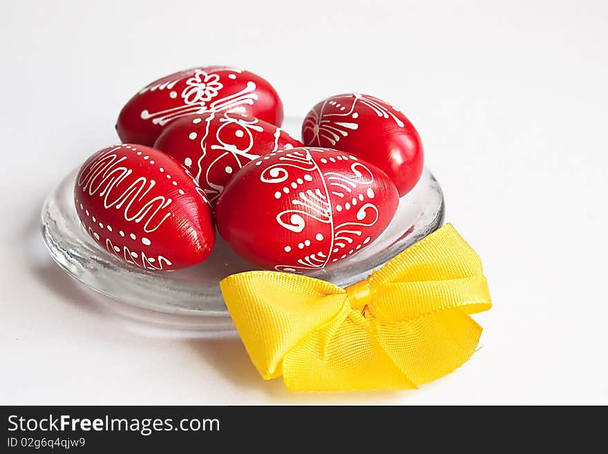 Red Easter eggs on a glass plate with yellow ribbon on white background. Red Easter eggs on a glass plate with yellow ribbon on white background