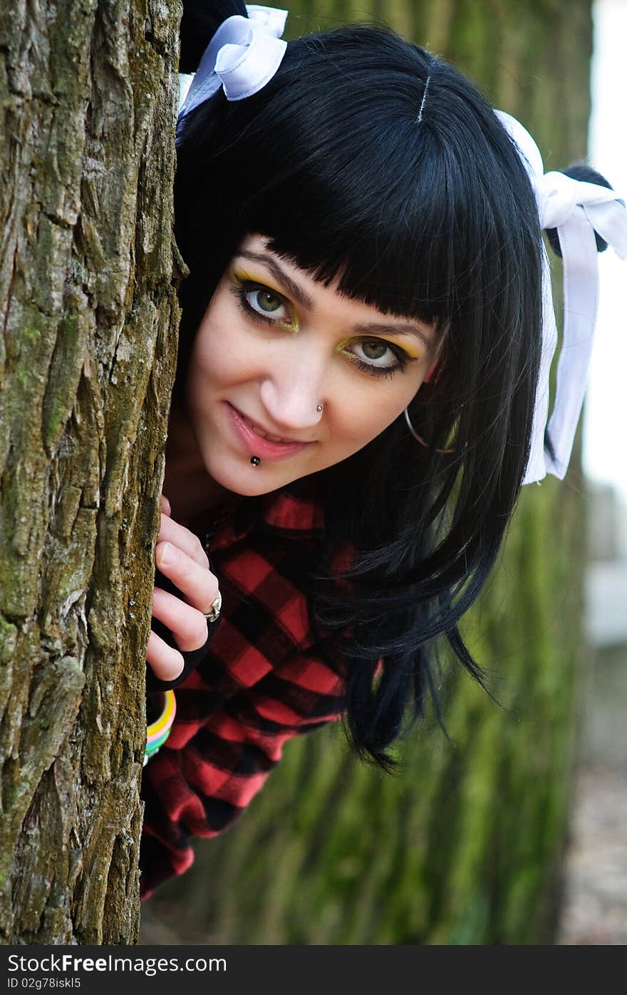 Beautiful girl looks out from behind a tree with a smile