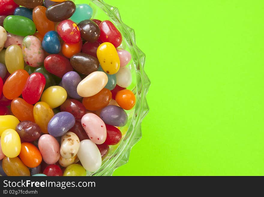 Pastel and bright jelly beans in a glass dish, against a bright green background. Pastel and bright jelly beans in a glass dish, against a bright green background