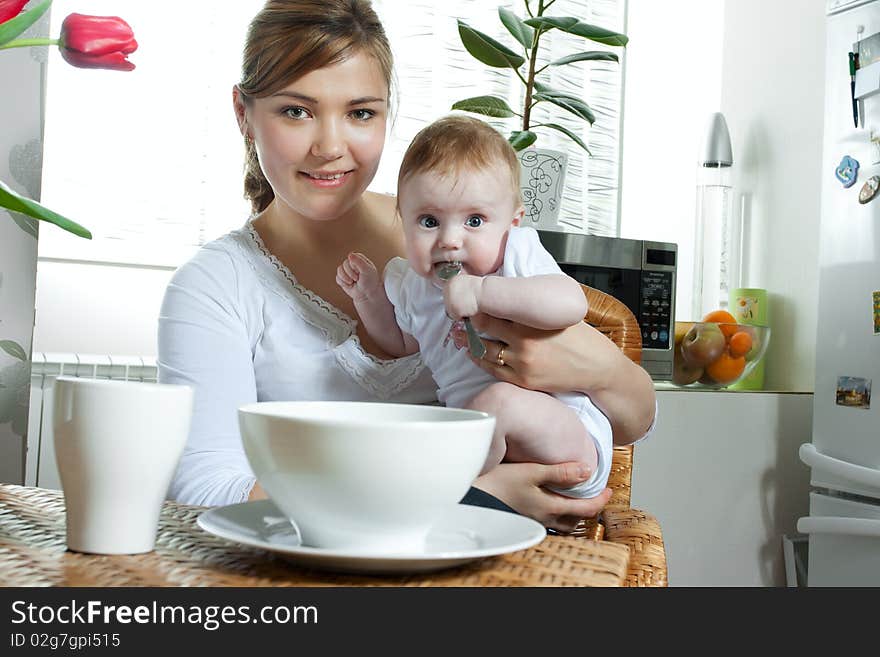 Young beautiful mother feeding her litlle cute baby daughter at the kitchen. Young beautiful mother feeding her litlle cute baby daughter at the kitchen