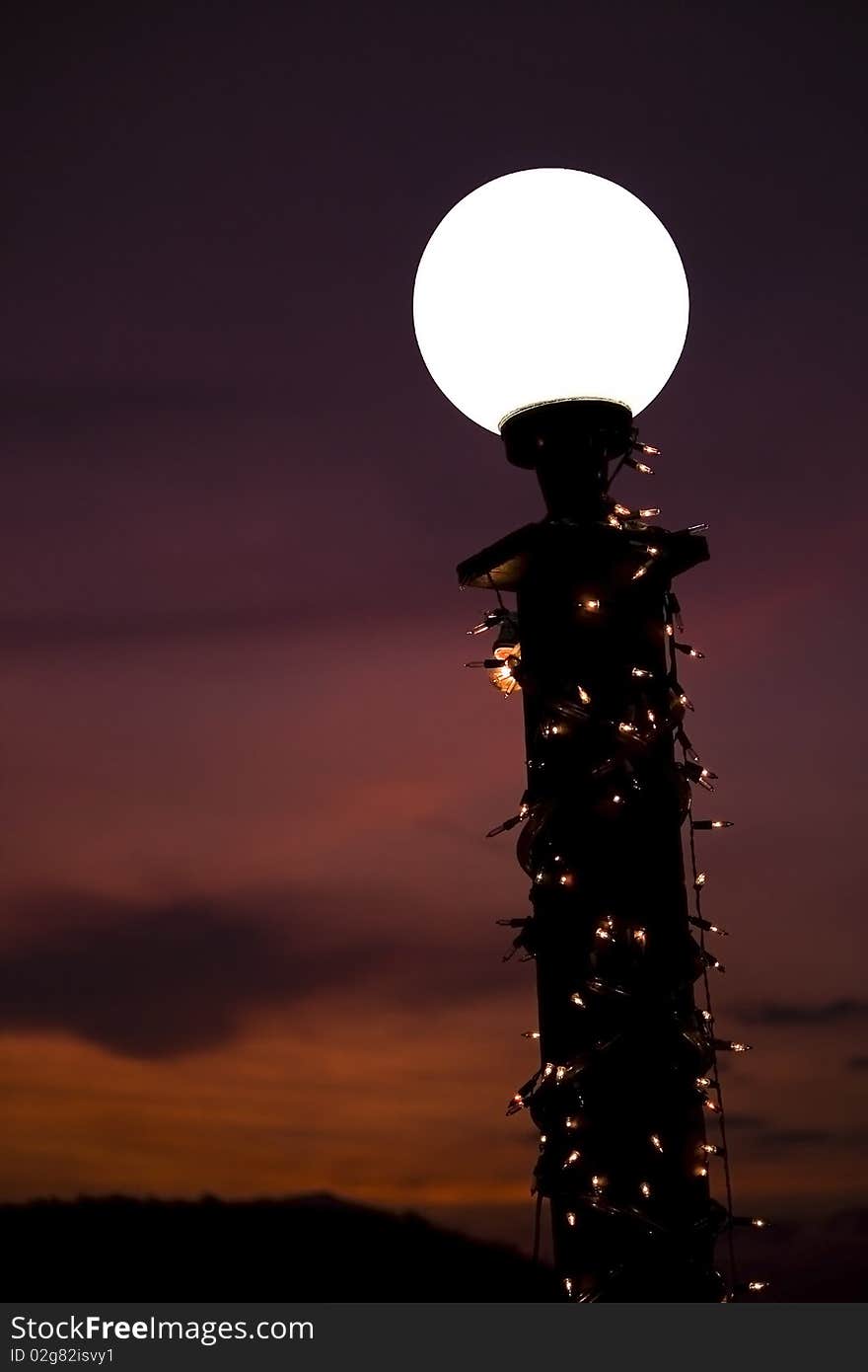 A white-light lamp decorated with light bulbs in front of a sunset background. A white-light lamp decorated with light bulbs in front of a sunset background