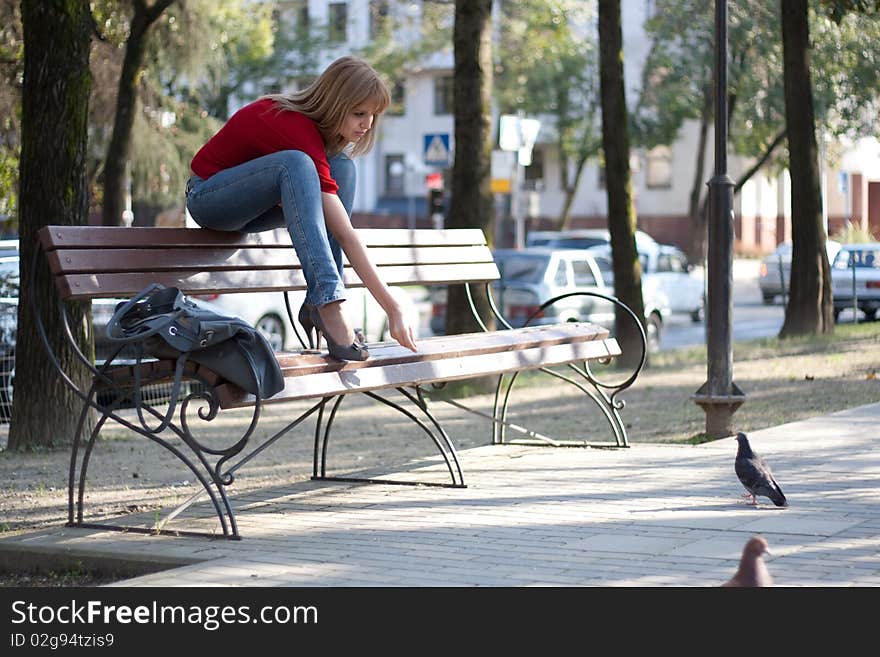 A beautiful girl sits on the back of bench and feeds a pigeon. A beautiful girl sits on the back of bench and feeds a pigeon.