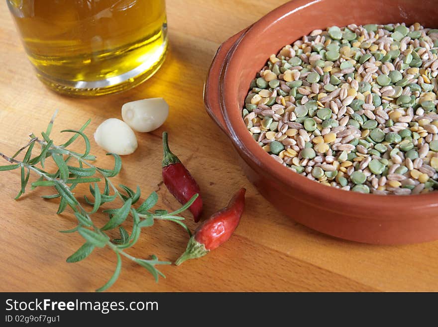 A bowl of raw mixed legumes, with olive oil, garlic, chilli peppers and fresh rosemary on a wooden board. A bowl of raw mixed legumes, with olive oil, garlic, chilli peppers and fresh rosemary on a wooden board