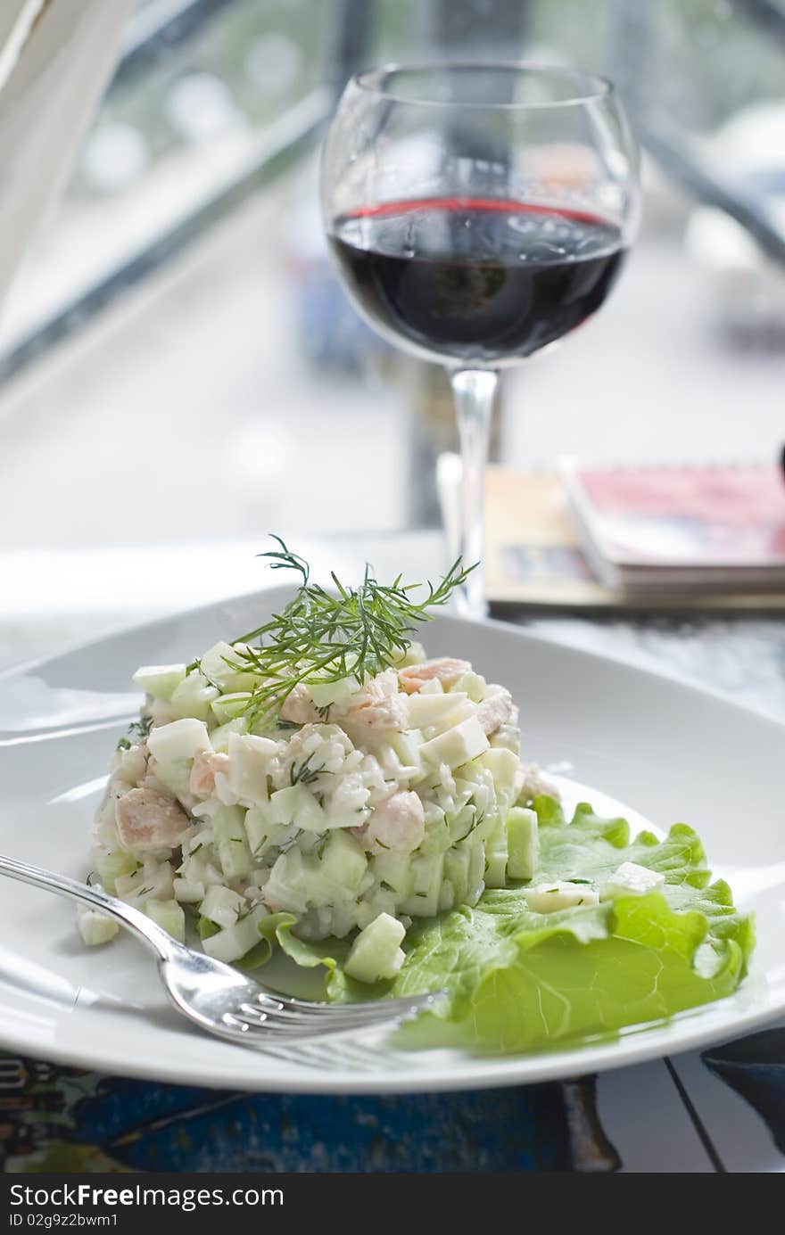 On the table in a restaurant is a plate with salad and a glass of red wine. On the table in a restaurant is a plate with salad and a glass of red wine