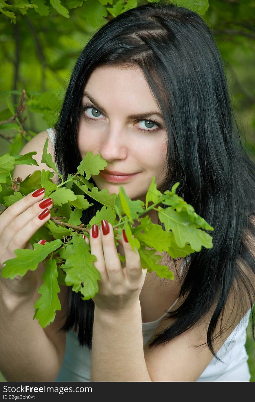 Young woman in forest touches oak leaves.