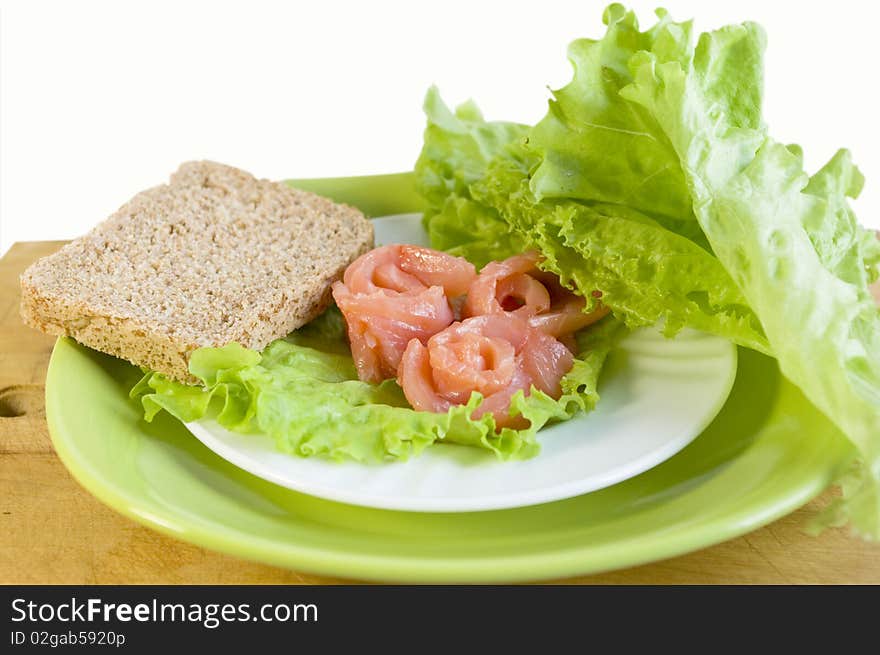 Salmon, bread and salad leaves on a white plate