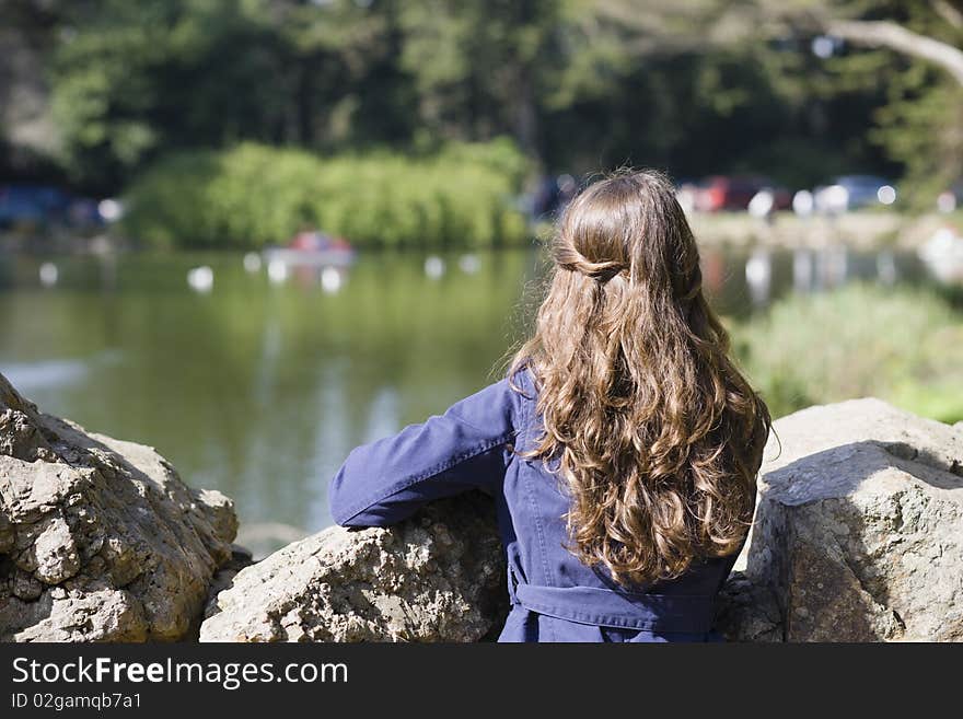 Back of a Woman With Long Brown Hair Looking Over Rocks at a Pond. Back of a Woman With Long Brown Hair Looking Over Rocks at a Pond