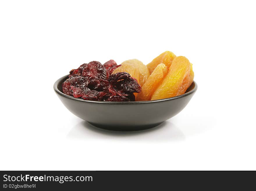 Red ripe dried cranberries and dried apricots in a small black bowl on a reflective white background. Red ripe dried cranberries and dried apricots in a small black bowl on a reflective white background