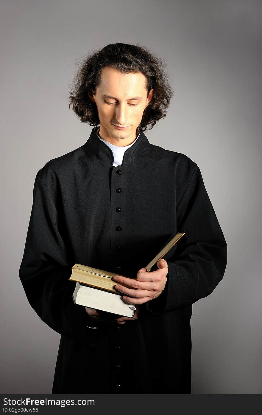 Conceptual portrait of Praying priest with wooden cross reading Holy Bible. yellow background