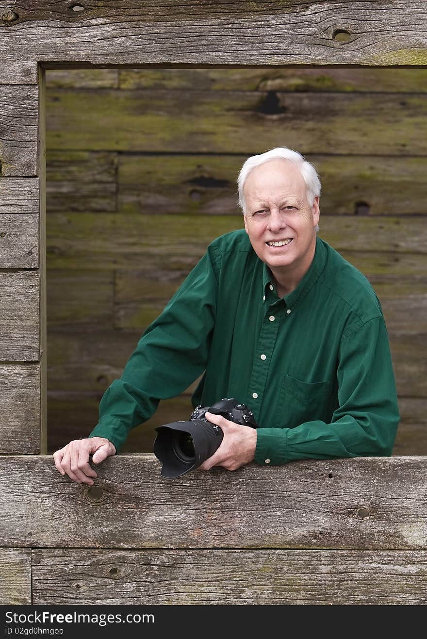 Senior mature man wearing green shirt posing for photograph inside barn window holding a camera. Senior mature man wearing green shirt posing for photograph inside barn window holding a camera.