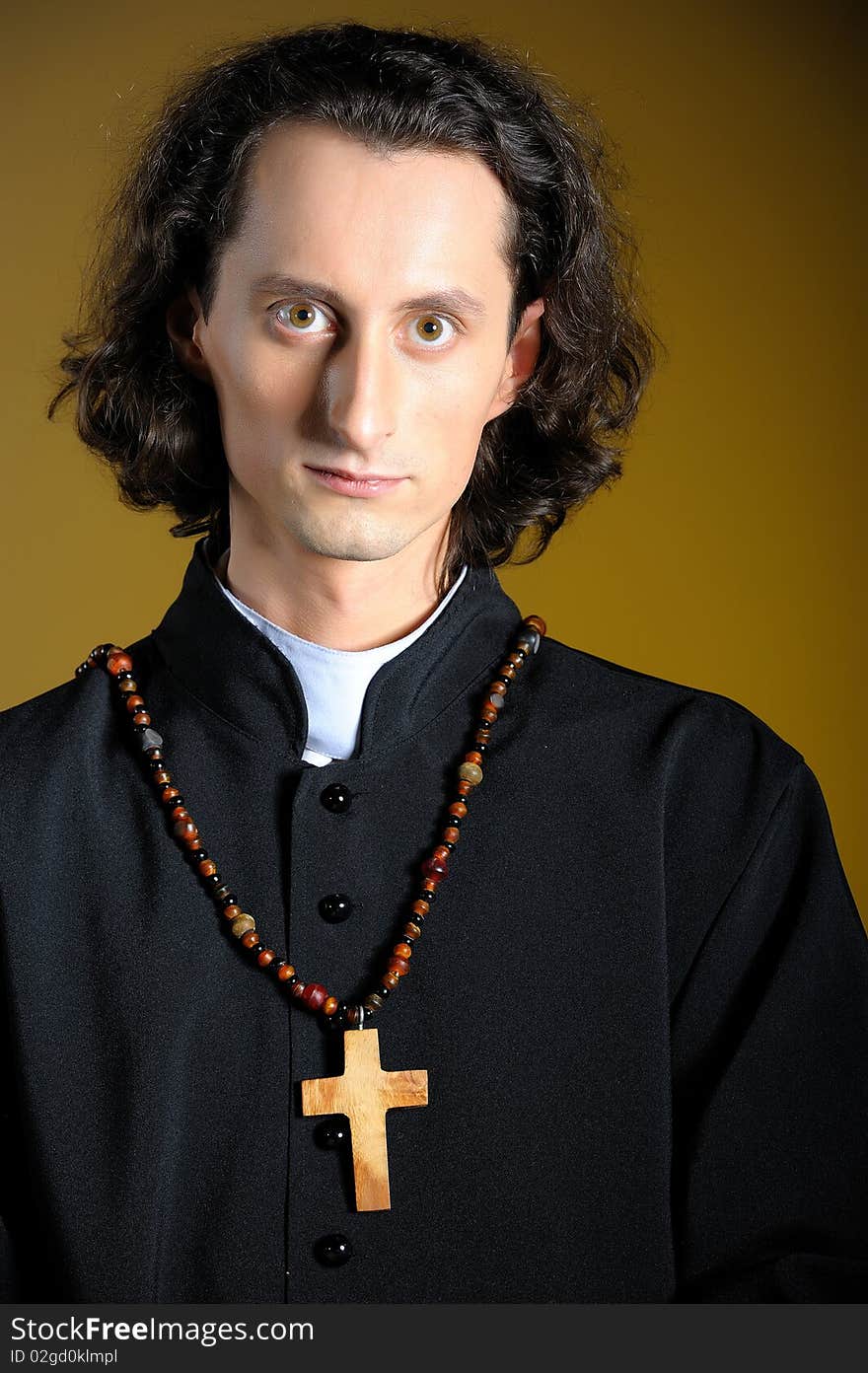 Conceptual portrait of Praying priest with wooden cross reading Holy Bible. yellow background