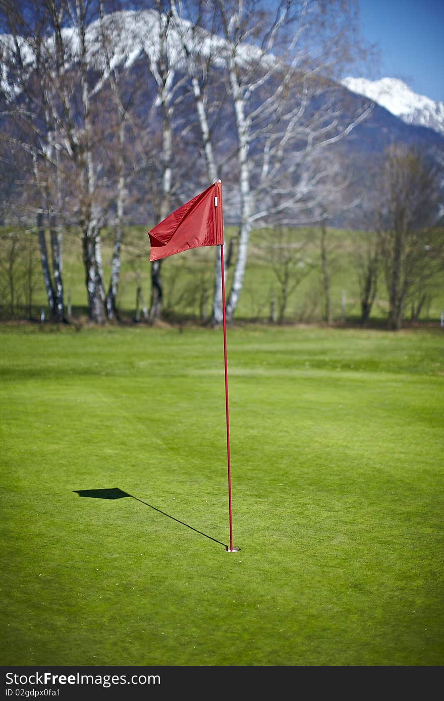 Red flag hole marker at the golf course with mountains in the back