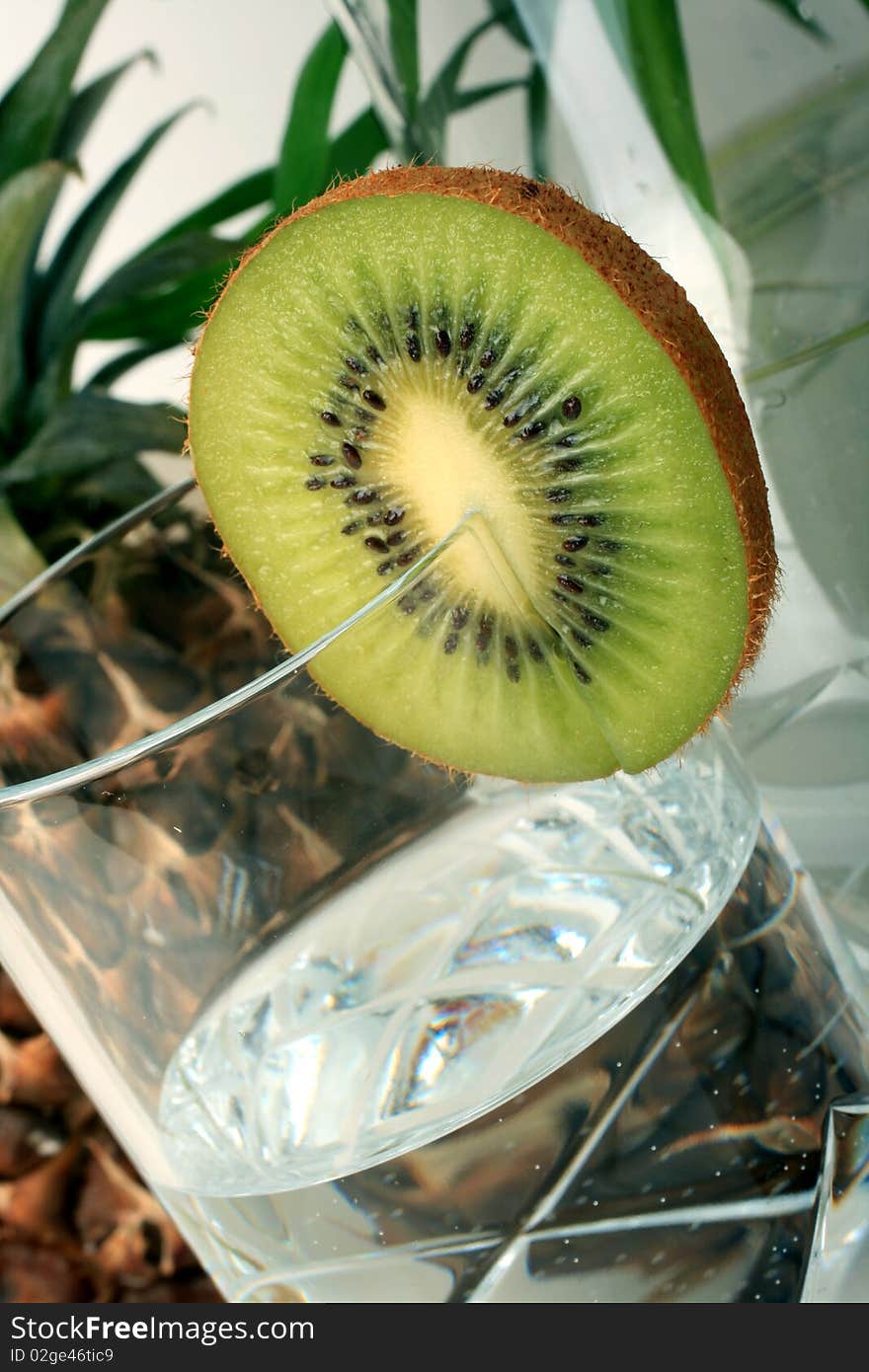 A slice kiwi with mineral water , pineapple background