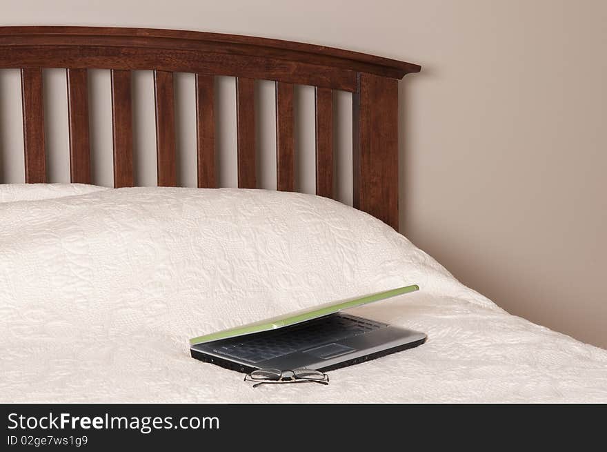 Laptop computer on a bed with a pair of glasses. Working from home concept.