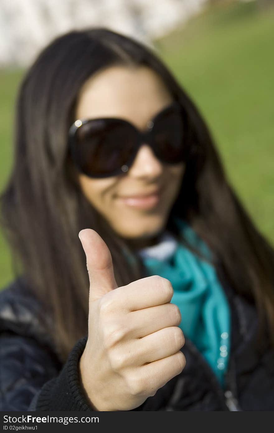 A beautiful young brunette girl in a park sitting on a bench smiling. Thumb sign OK. A beautiful young brunette girl in a park sitting on a bench smiling. Thumb sign OK