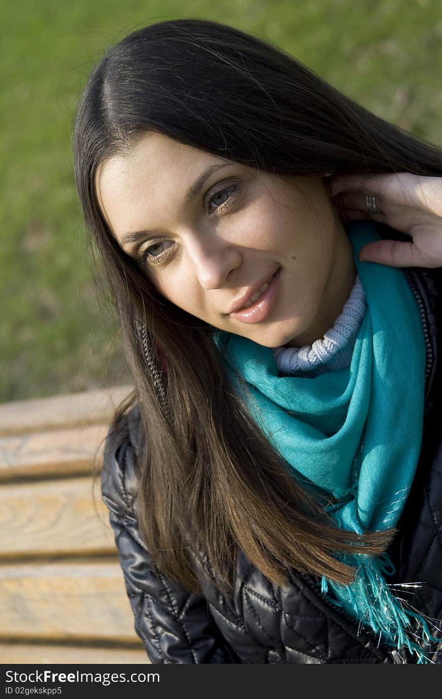 A beautiful young brunette girl in a park sitting on a bench smiling. A beautiful young brunette girl in a park sitting on a bench smiling