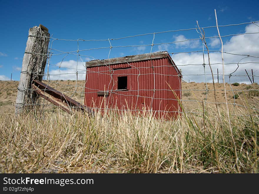 Rural landscape with small red shed viewed through wire mesh fence. Rural landscape with small red shed viewed through wire mesh fence.