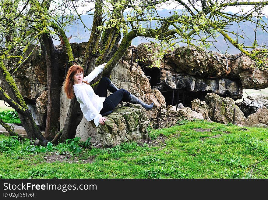 Redheaded gorgeous girl sitting between tree and stone. Redheaded gorgeous girl sitting between tree and stone