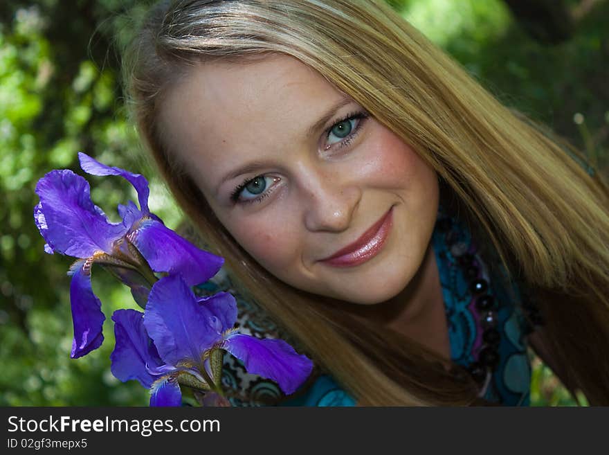 Portrait of the fair-haired girl in a garden with lilac flowers of an iris on a bed