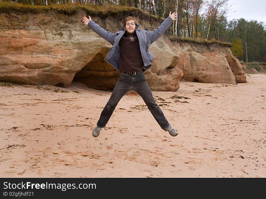 Beautiful young man is jumping on the beach near the caves. Beautiful young man is jumping on the beach near the caves.